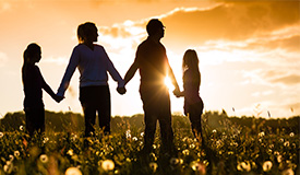 Familj som står i solnedgången och håller varandra i hand
